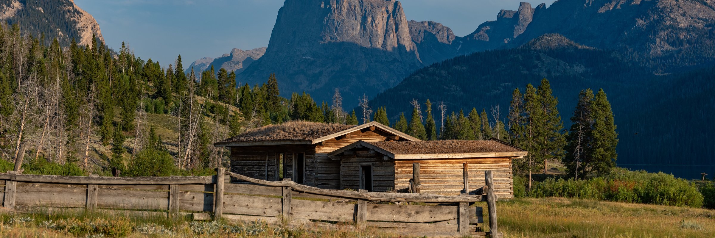 A weathered log homestead in a meadow with Squaretop Mountain rising in the background, Wind River Range, Wyoming
